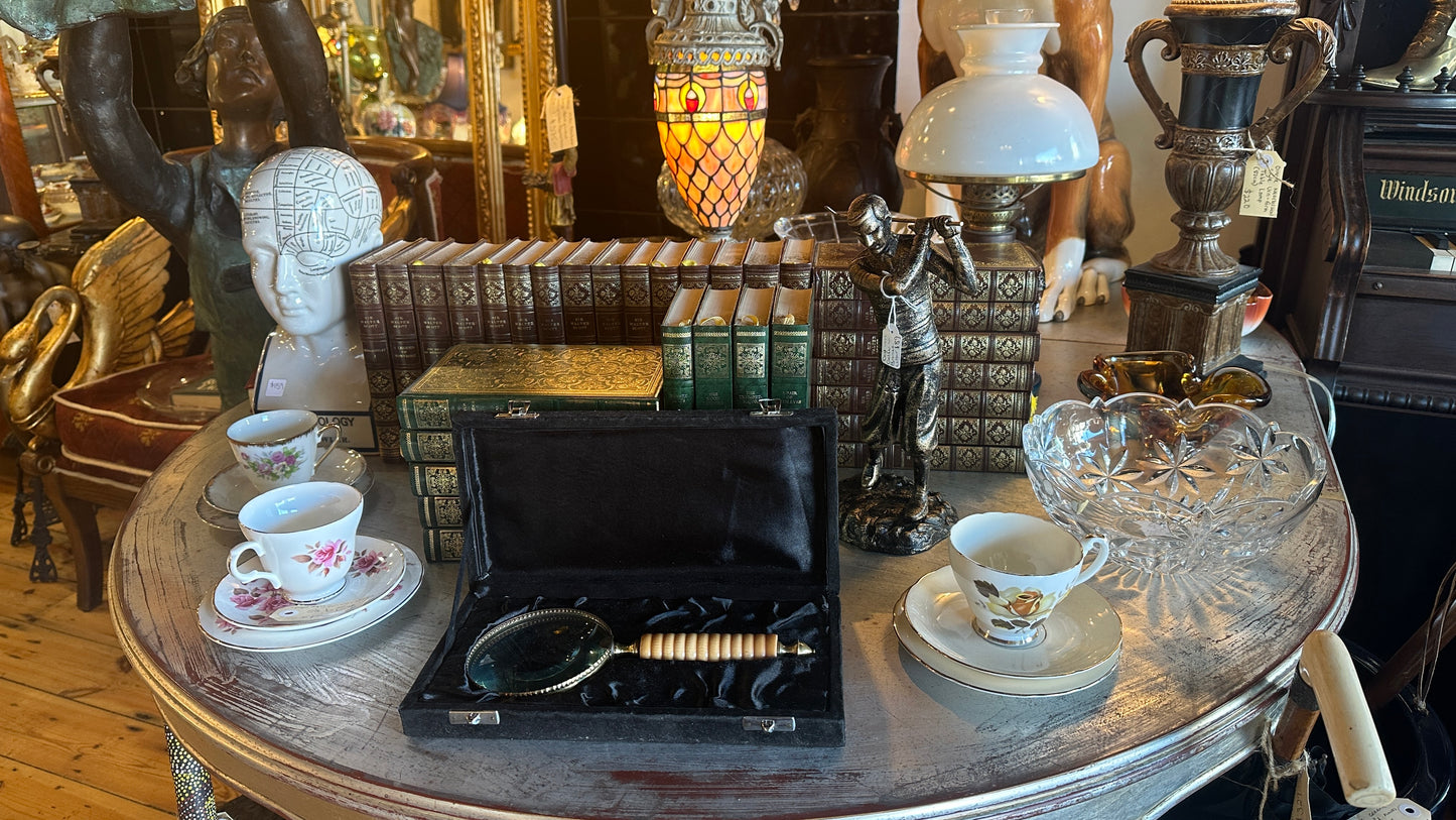 Vintage large brass and ribbed bone-style resin handle magnifying glass rests inside a black satin-lined presentation box