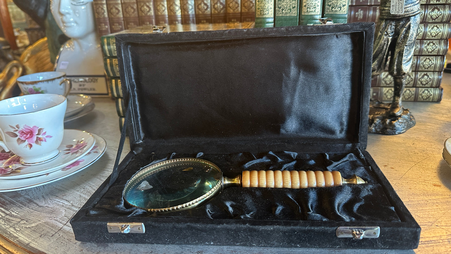 Vintage large brass and ribbed bone-style resin handle magnifying glass rests inside a black satin-lined presentation box