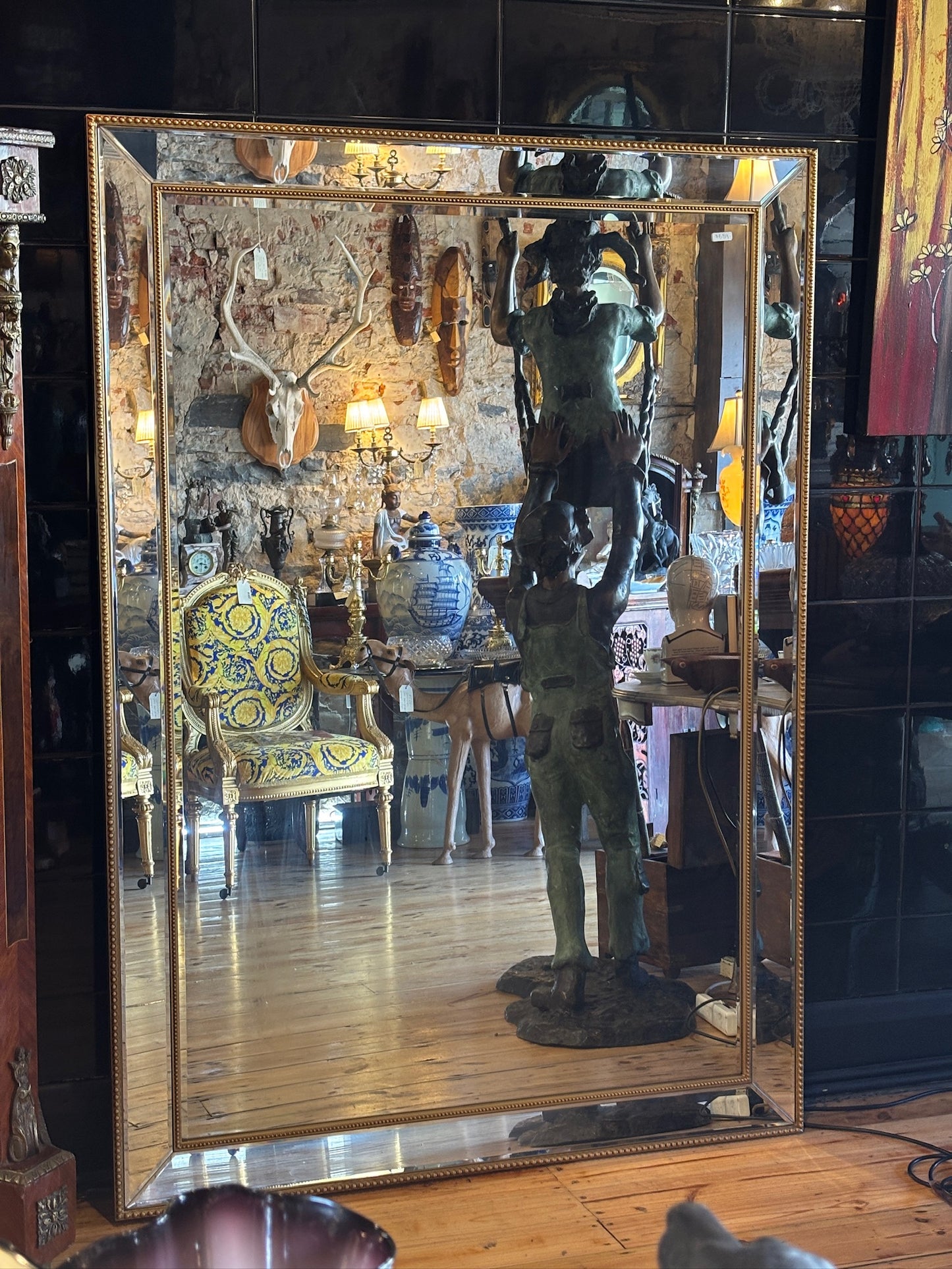 Large mirror features a classic bevel-edged glass pane set within a slender gold-beaded wooden frame