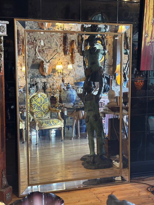 Large mirror features a classic bevel-edged glass pane set within a slender gold-beaded wooden frame