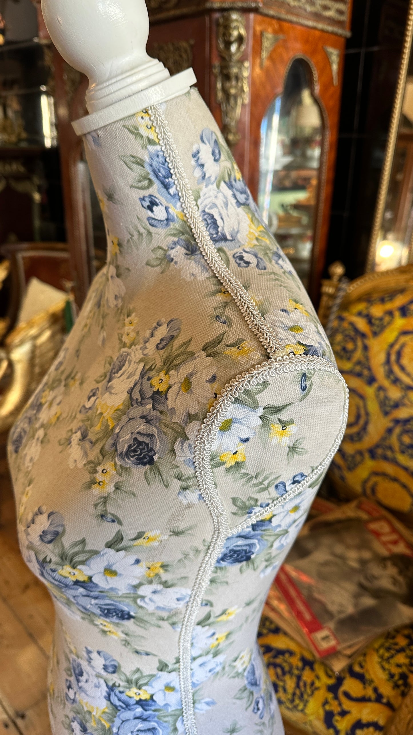 Decorative dressmaker's mannequin featuring a blue and yellow floral fabric print on a white tripod wooden stand