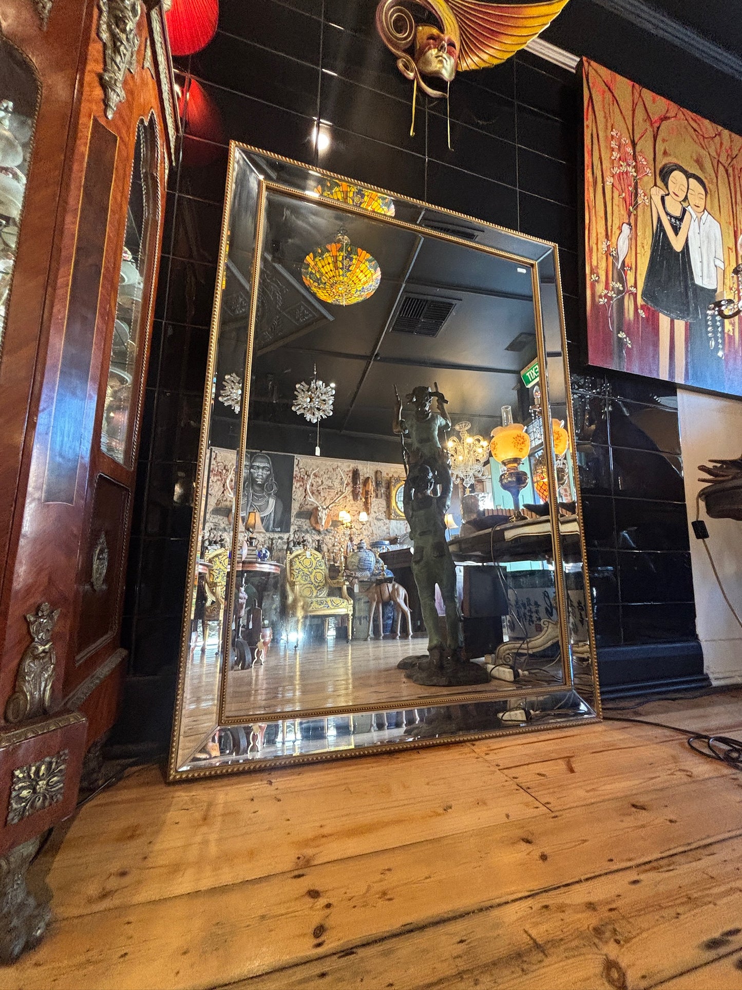Large mirror features a classic bevel-edged glass pane set within a slender gold-beaded wooden frame