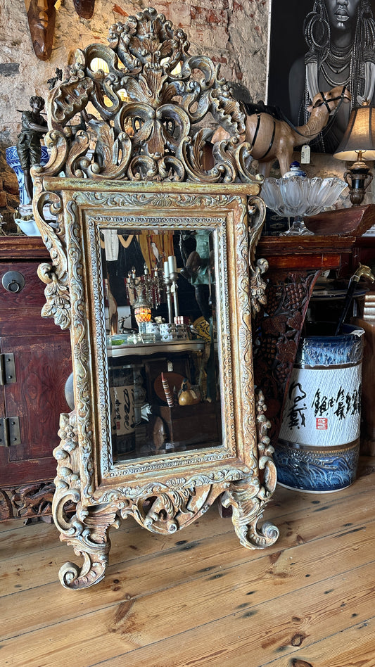 Ornate wall mirror featuring a distressed or painted finish in a Baroque or Rococo style