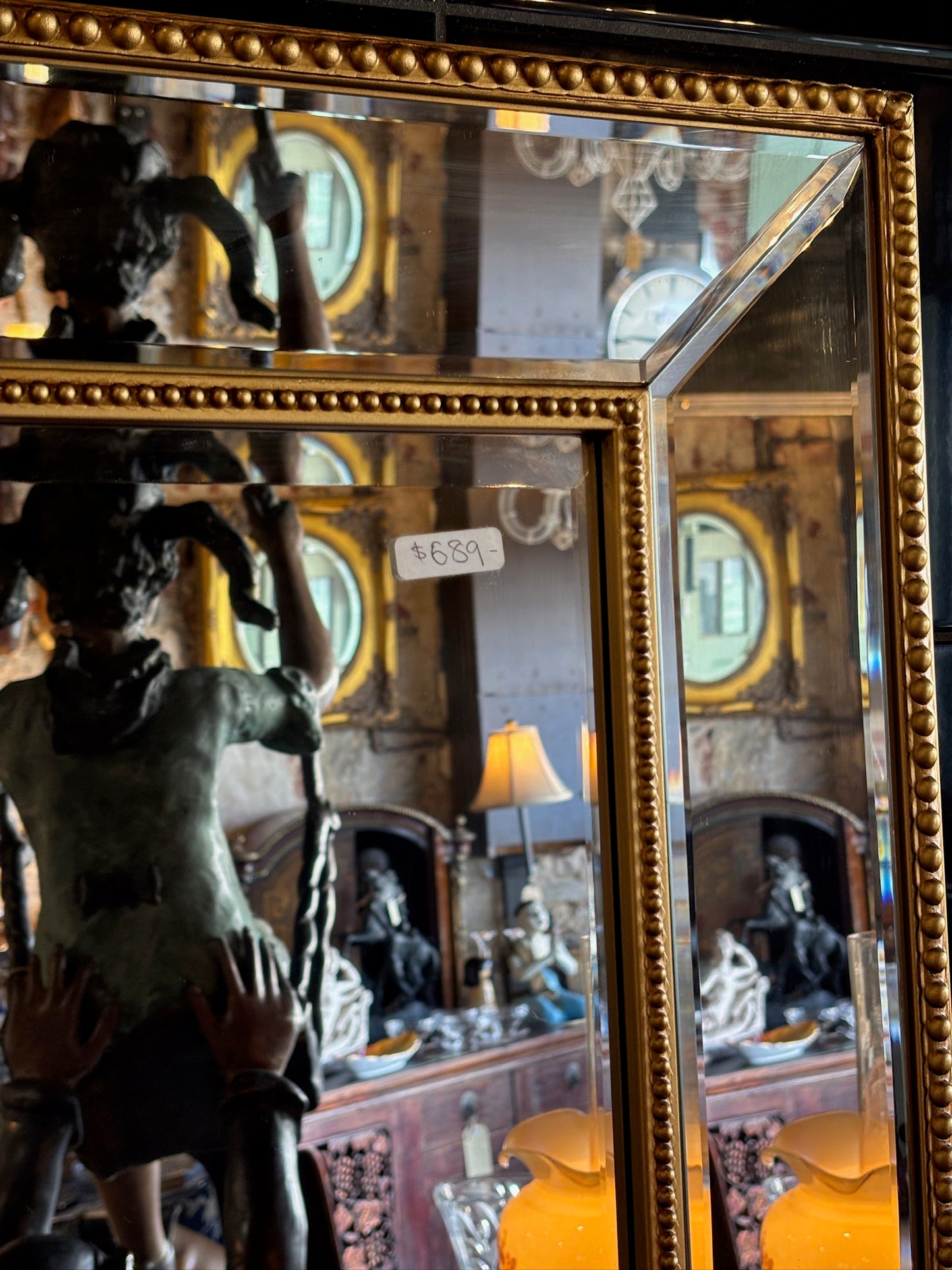 Large mirror features a classic bevel-edged glass pane set within a slender gold-beaded wooden frame