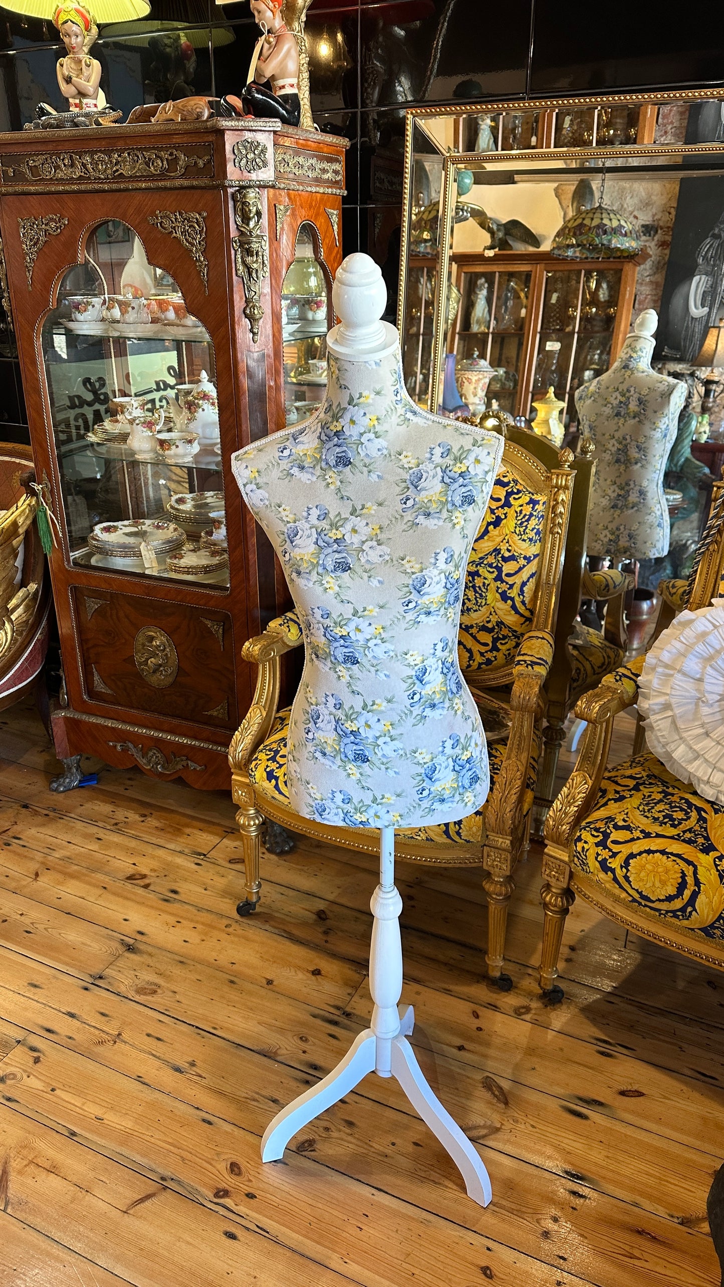 Decorative dressmaker's mannequin featuring a blue and yellow floral fabric print on a white tripod wooden stand