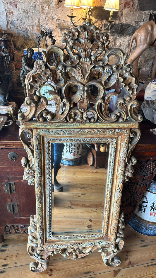 Ornate wall mirror featuring a distressed or painted finish in a Baroque or Rococo style