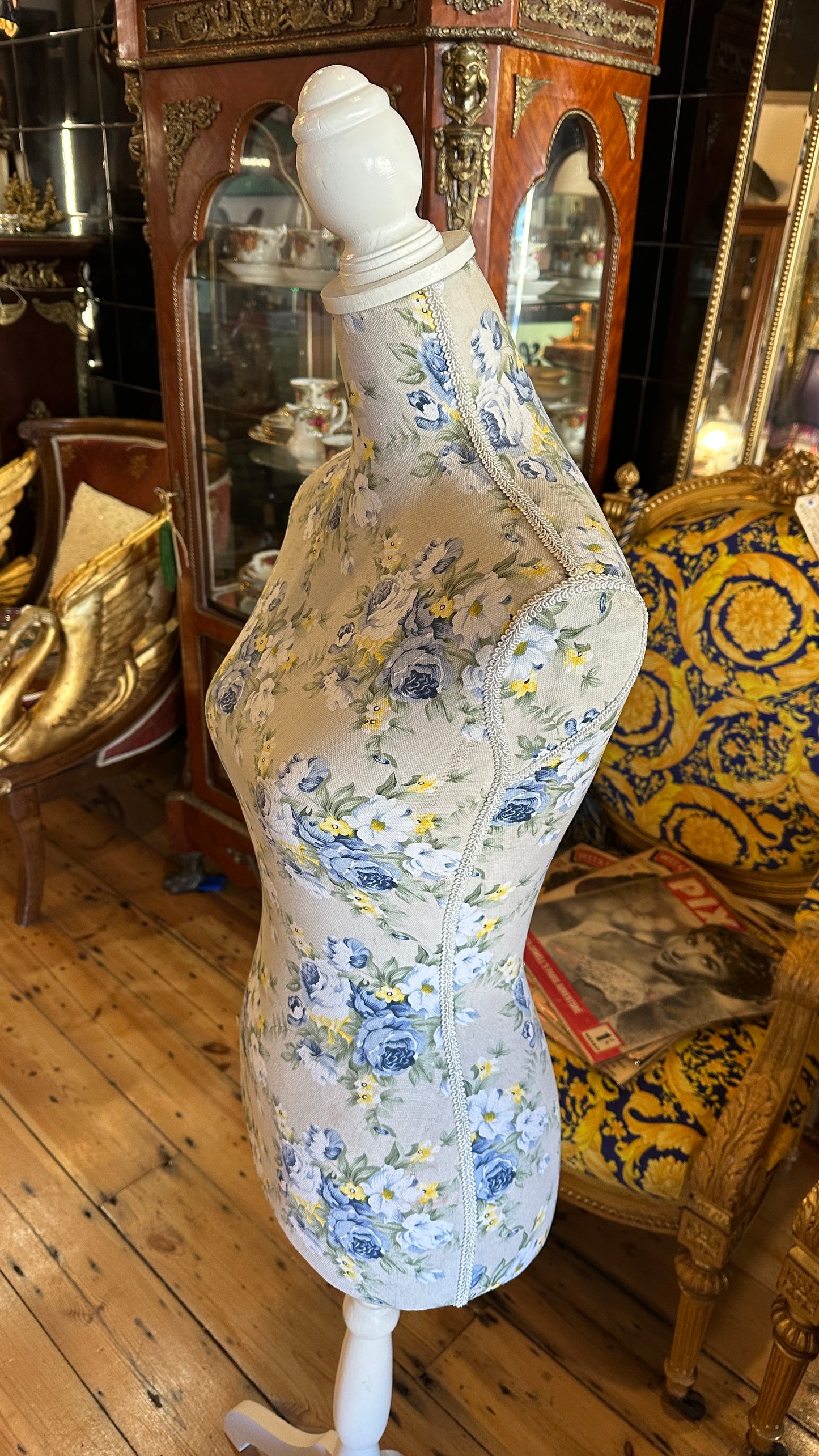 Decorative dressmaker's mannequin featuring a blue and yellow floral fabric print on a white tripod wooden stand