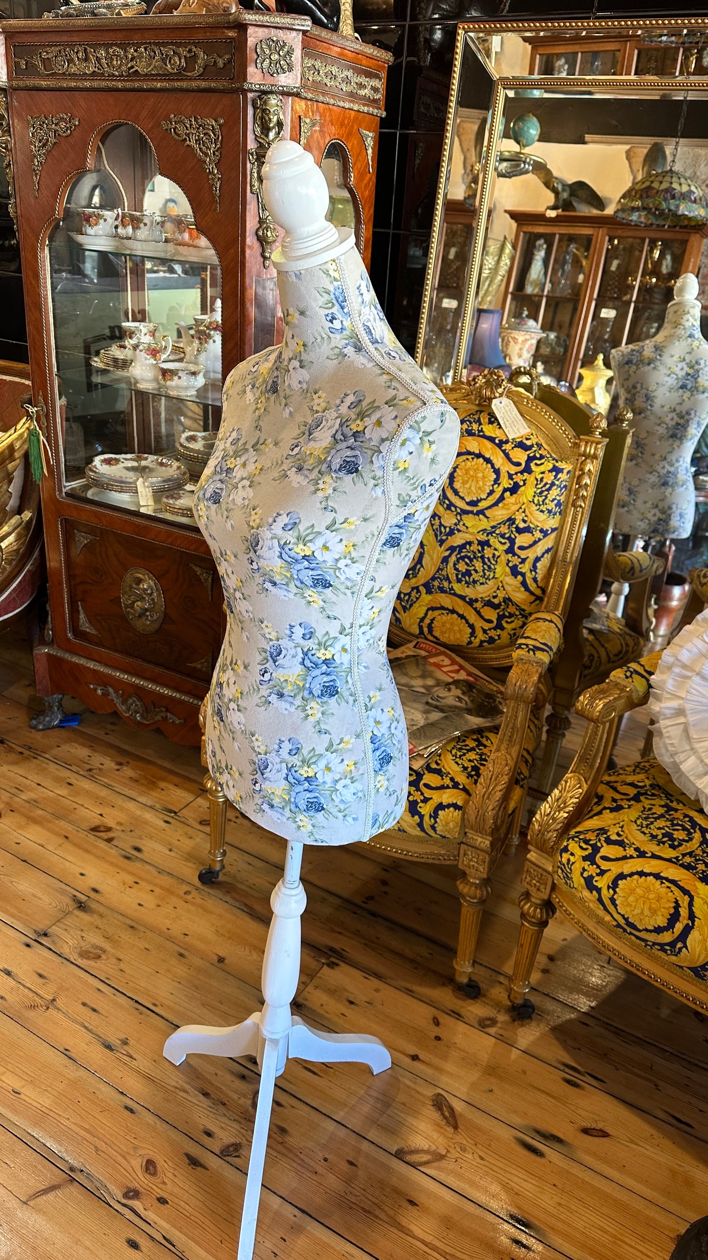 Decorative dressmaker's mannequin featuring a blue and yellow floral fabric print on a white tripod wooden stand