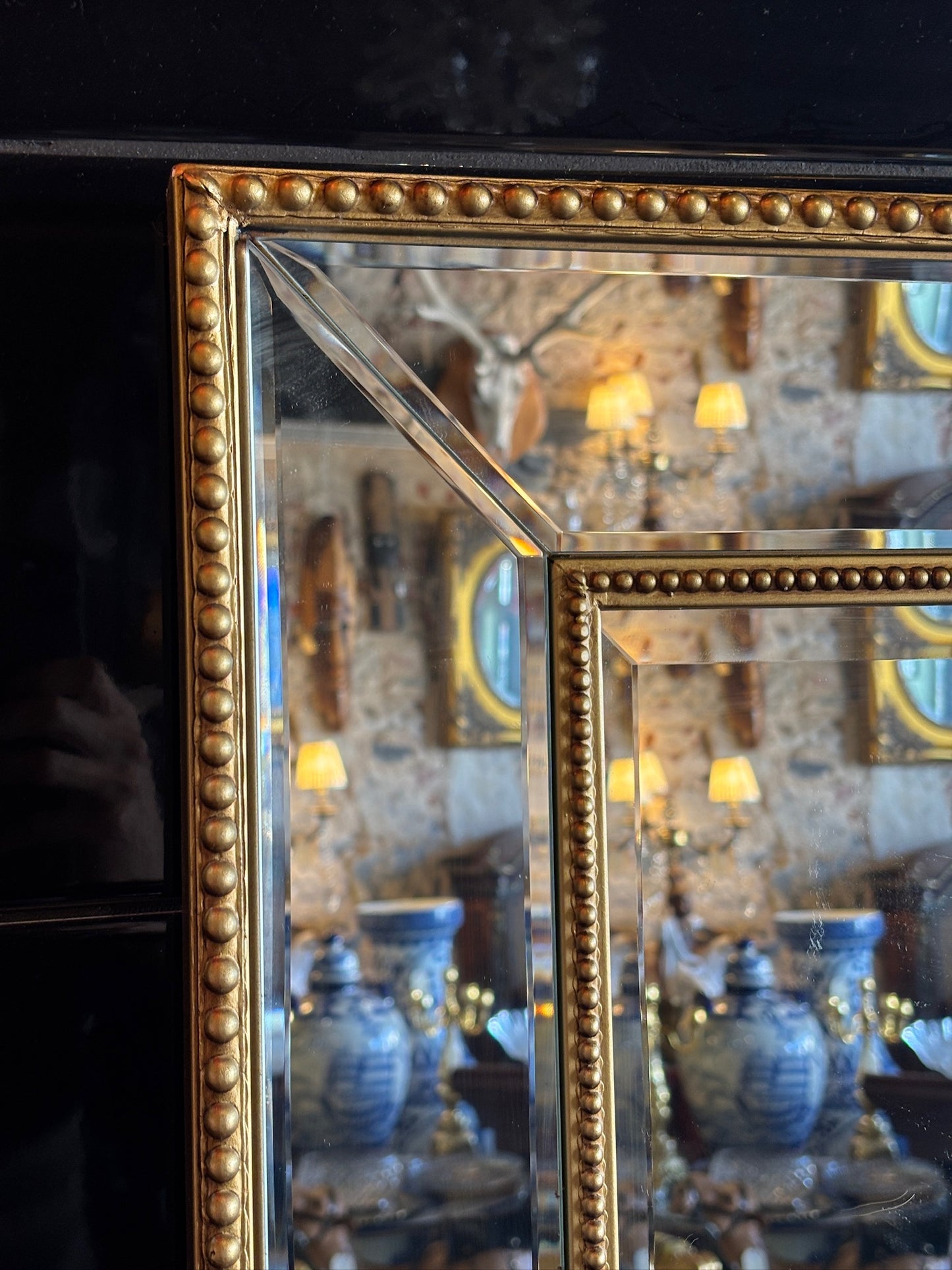 Large mirror features a classic bevel-edged glass pane set within a slender gold-beaded wooden frame
