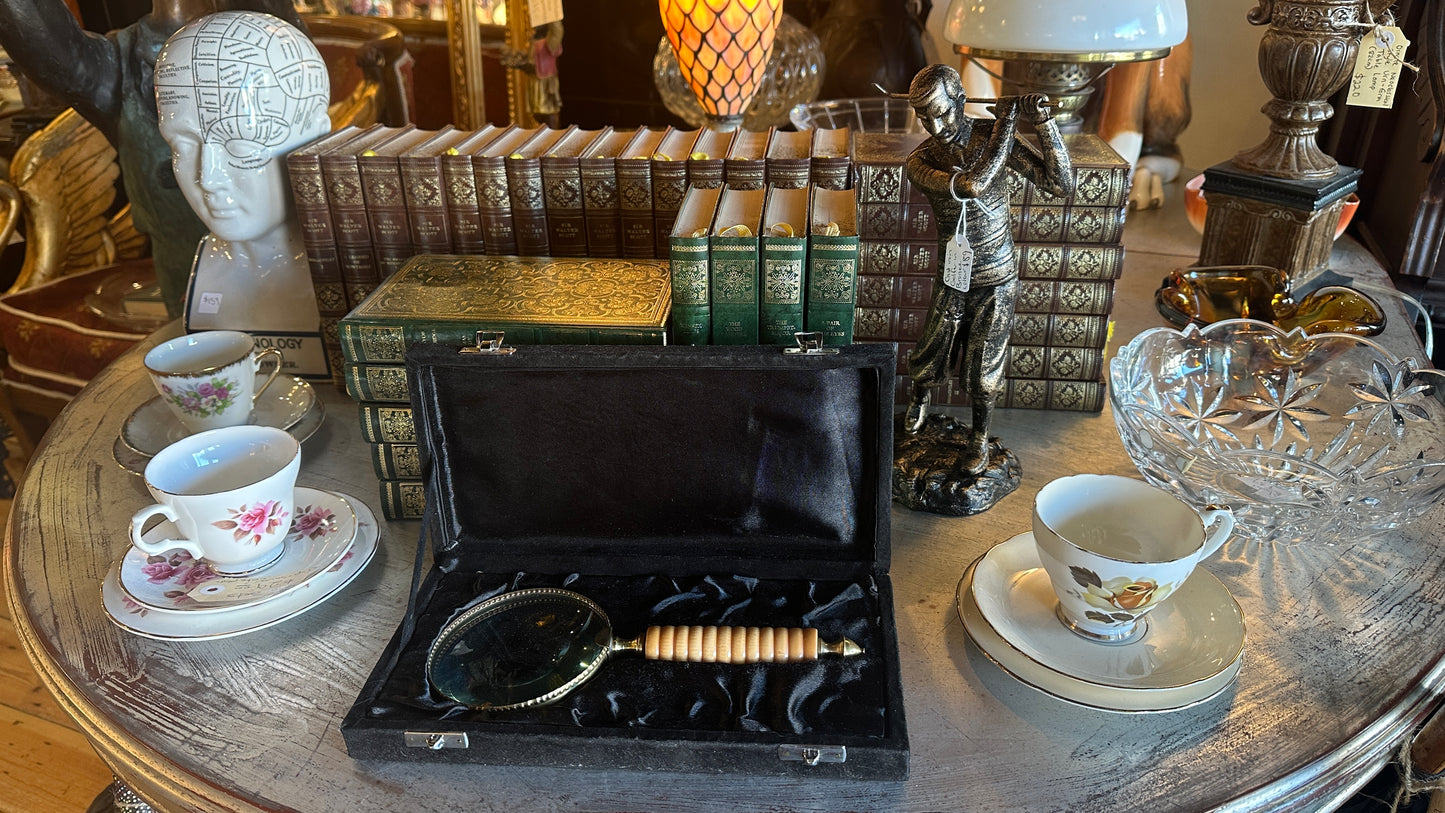 Vintage large brass and ribbed bone-style resin handle magnifying glass rests inside a black satin-lined presentation box