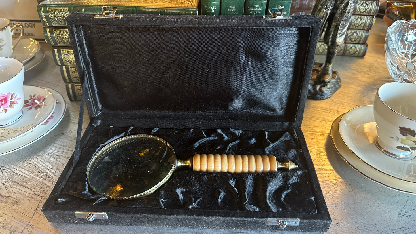 Vintage large brass and ribbed bone-style resin handle magnifying glass rests inside a black satin-lined presentation box