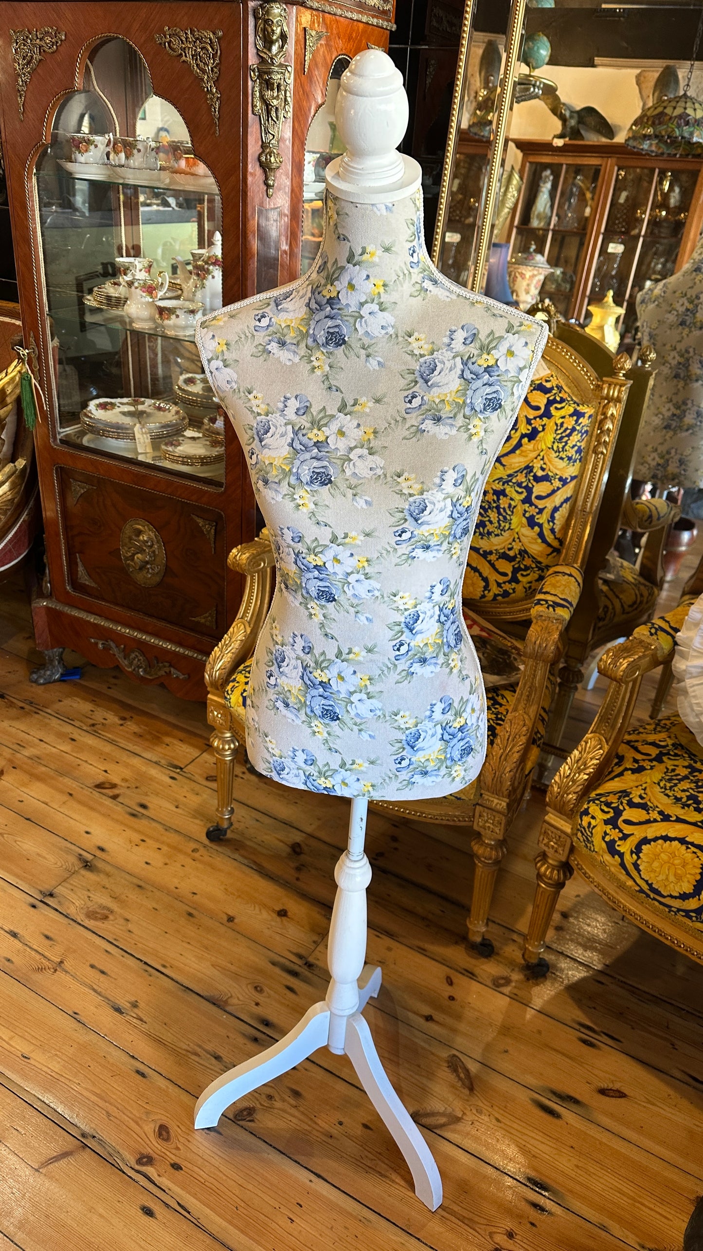 Decorative dressmaker's mannequin featuring a blue and yellow floral fabric print on a white tripod wooden stand