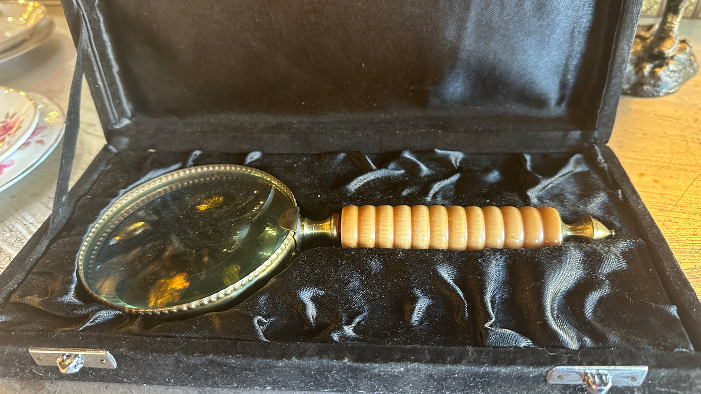 Vintage large brass and ribbed bone-style resin handle magnifying glass rests inside a black satin-lined presentation box